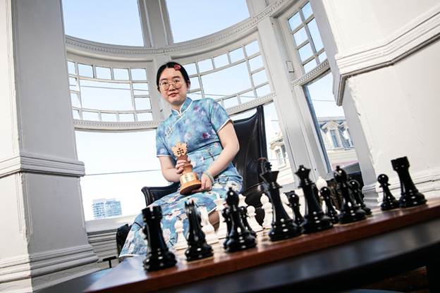 A person sitting in a chair holding a chess piece
Description automatically generated